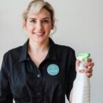 Professionnelle souriante tenant un produit de nettoyage, symbolisant un service de ménage écologique et fiable.